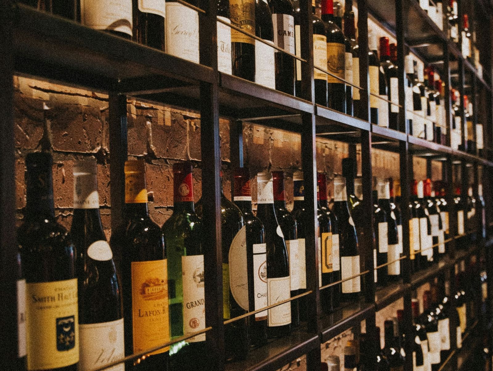 Shelves filled with a wide variety of wine bottles in a warmly lit cellar aisle.