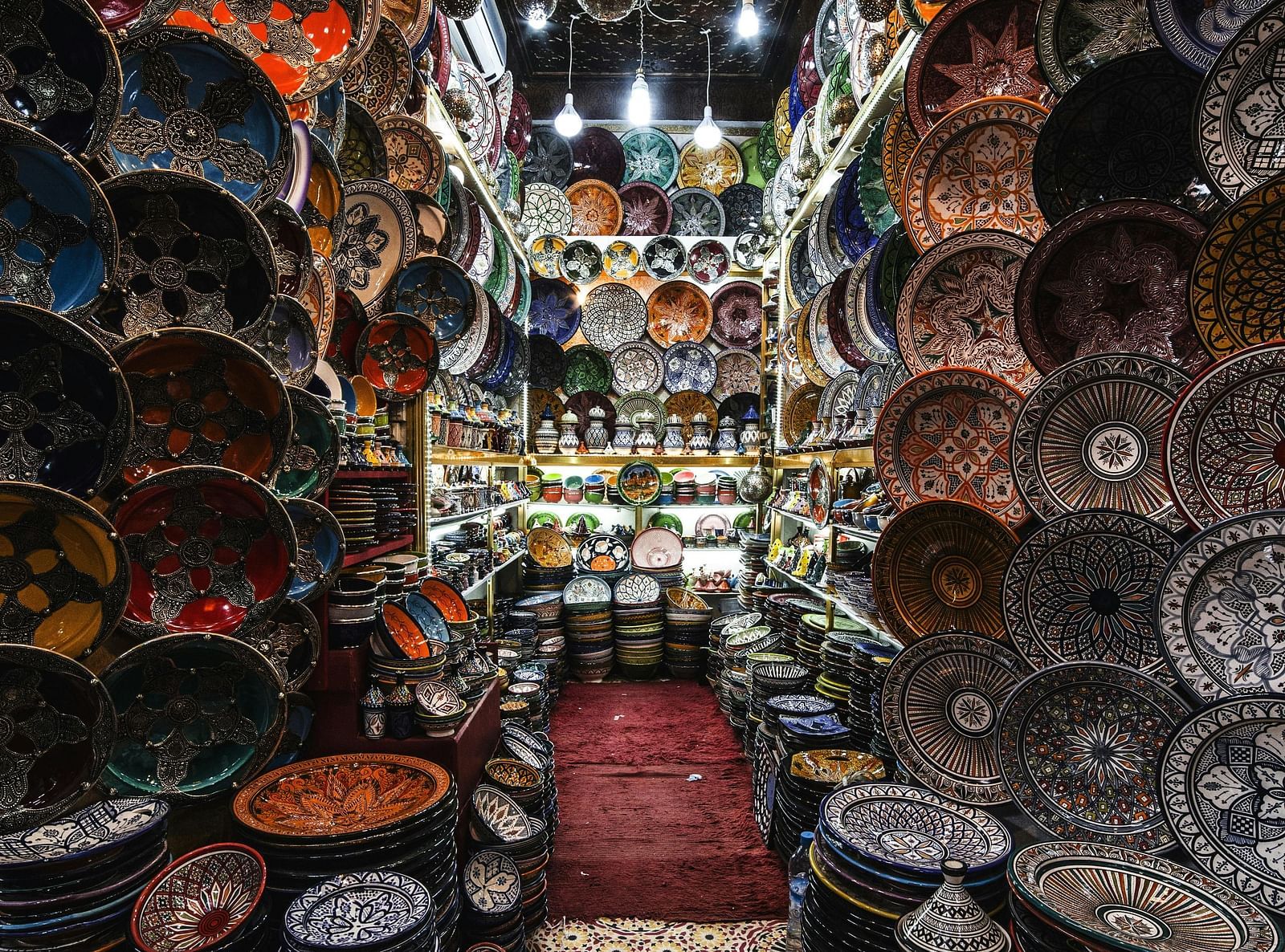 A narrow aisle in an Oriental shop, filled with colorful bowls, plates, and hanging lamps, creates a vibrant and immersive shopping experience.