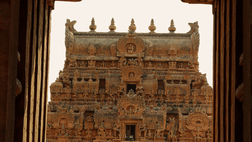 A view from inside a building of the entrance to Brihadeswara Temple in the distance with a pathway leading to the temple and people walking on it.