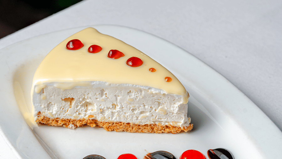 A slice of cheesecake with red glaze drops at Café Latte, part of the Noor-Us-Sabah Palace, Bhopal, served on a white plate with decorative sauces.