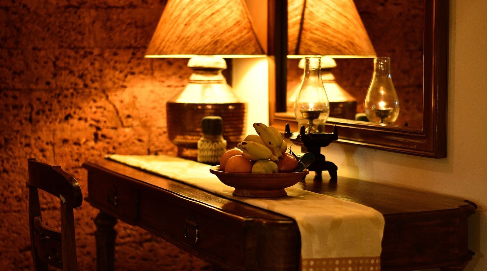 image of a study table with a basket full of fruits and a dimly lit table lamp at hoysala village resort in hassan