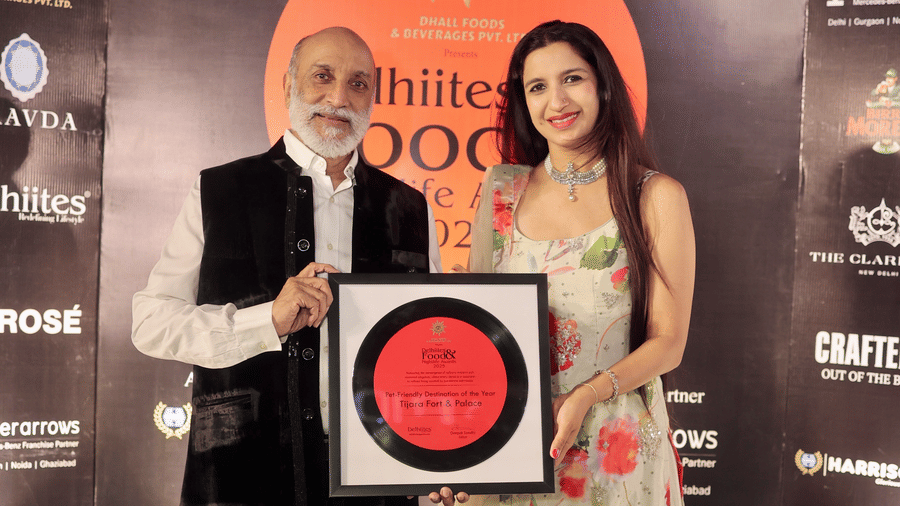 Two people posing with a framed award for 'Pet-Friendly Destination of the Year 2025' awarded to Tijara Fort & Palace at the Delhiites Food & Nightlife Awards.