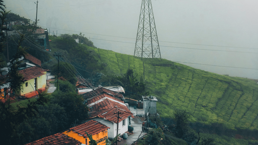 A vertical shot of a misty, green hillside featuring a few small houses and a large electricity pylon disappearing into heavy white fog.