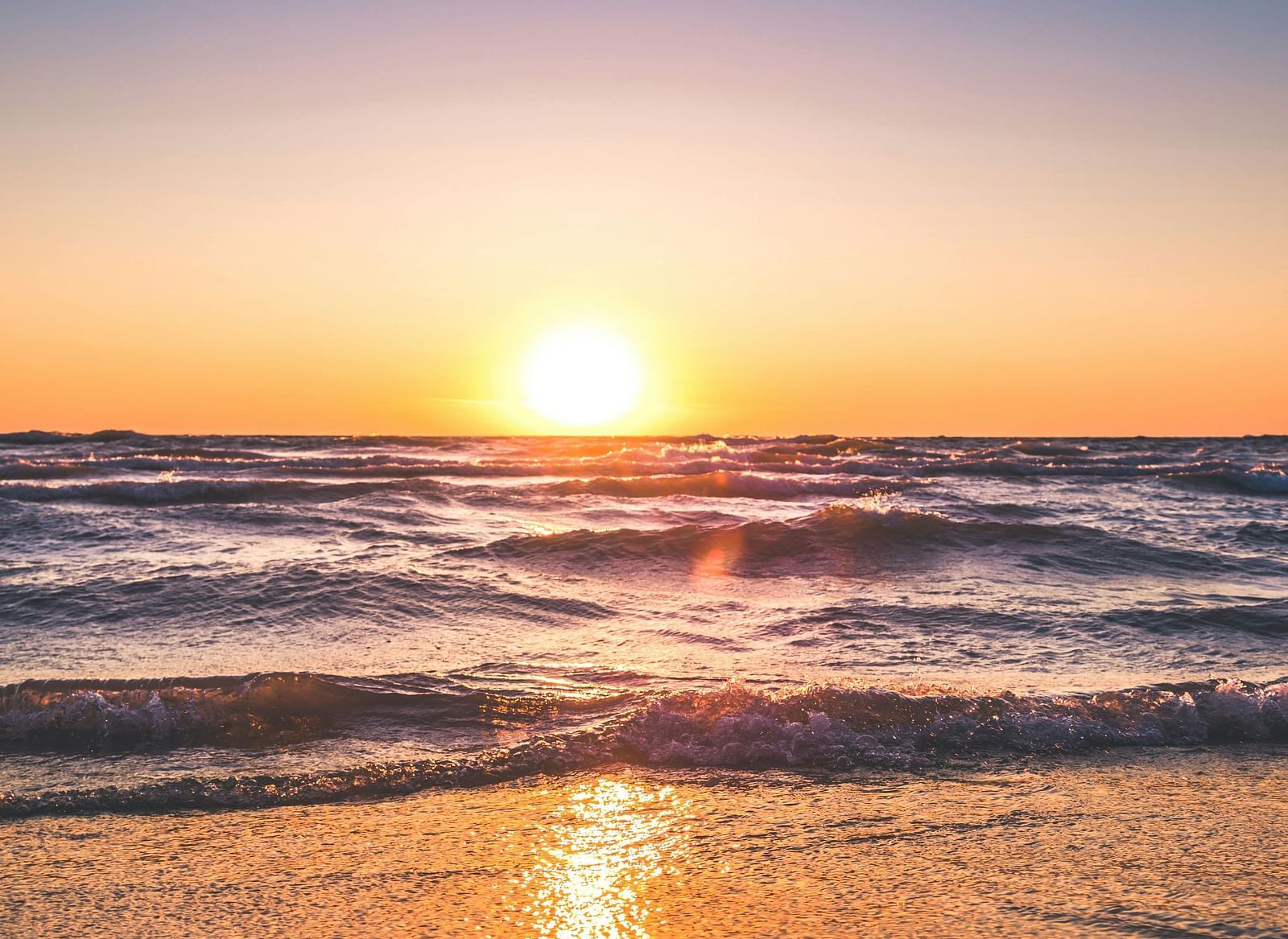  A stunning beach view at sunset, with the sun reflecting on the water and soft hues of orange and purple in the sky.
