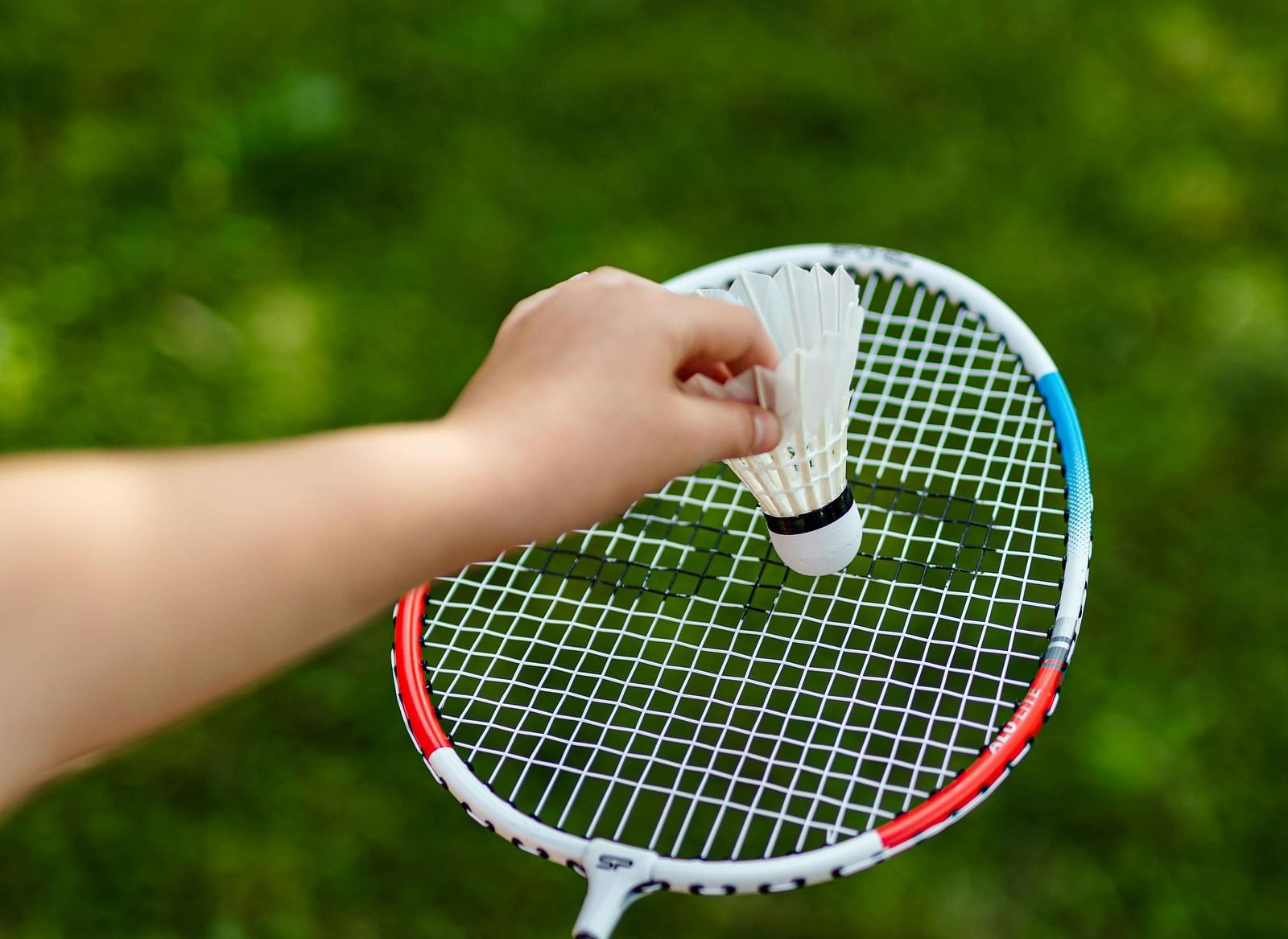 A person preparing to serve, holding a shuttlecock against a racket
