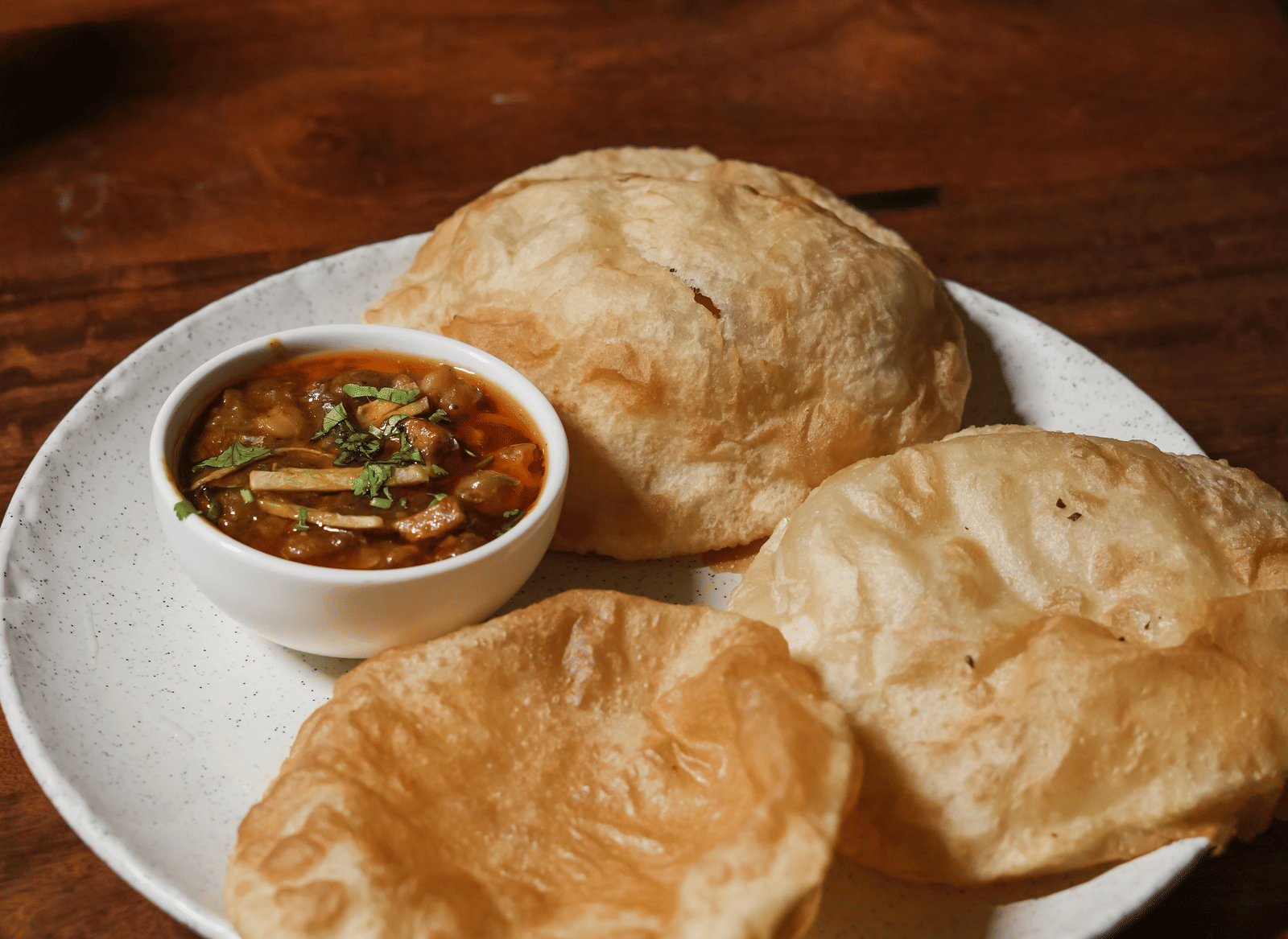 A dish of two golden-brown, puffed bhature breads served with a small bowl of chickpea curry (chole) on a white plate at BluSalzz Select City Centre, Amritsar.
