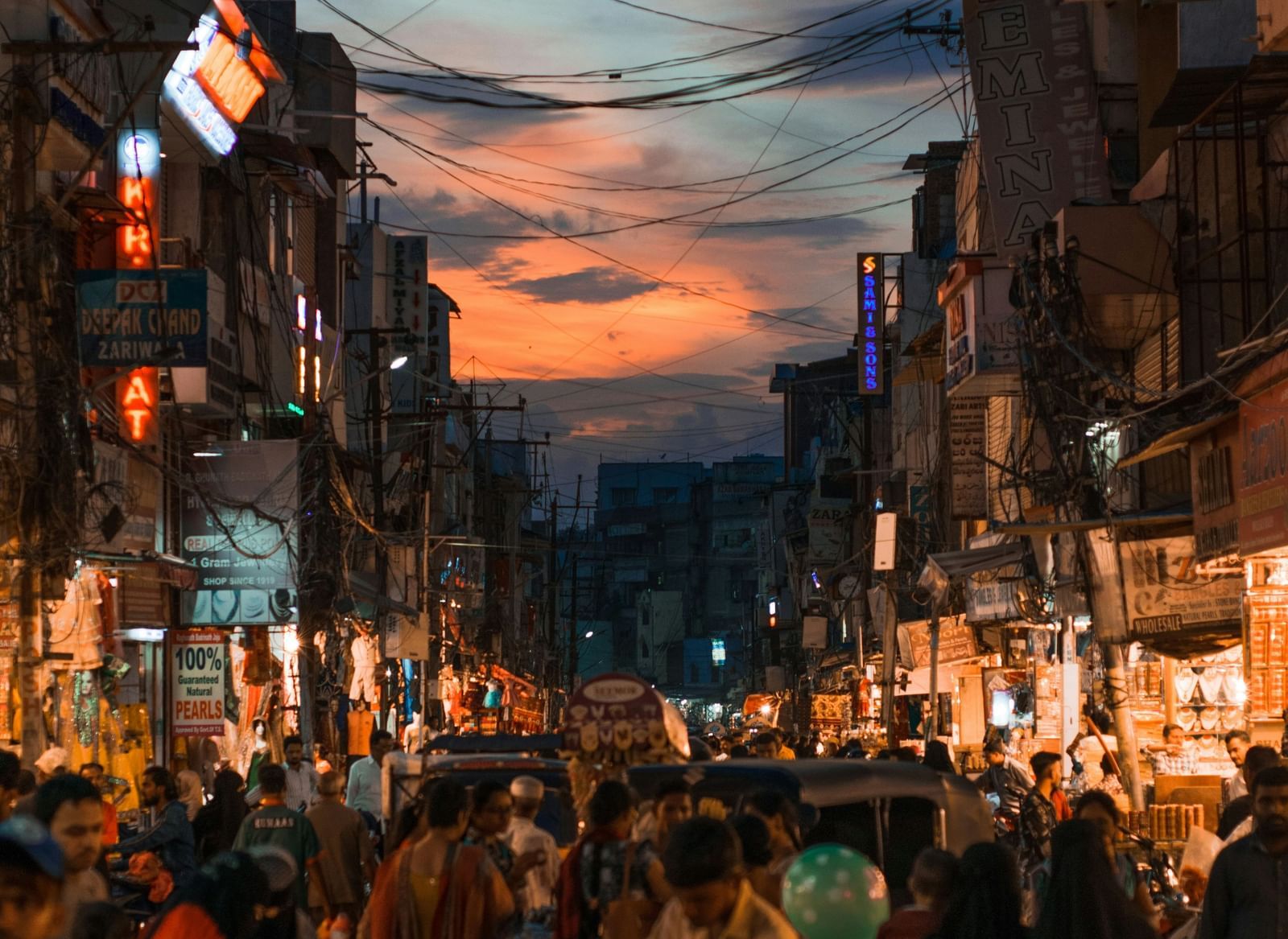 Crowded street scene at dusk or night with bright orange and blue lights hanging overhead.