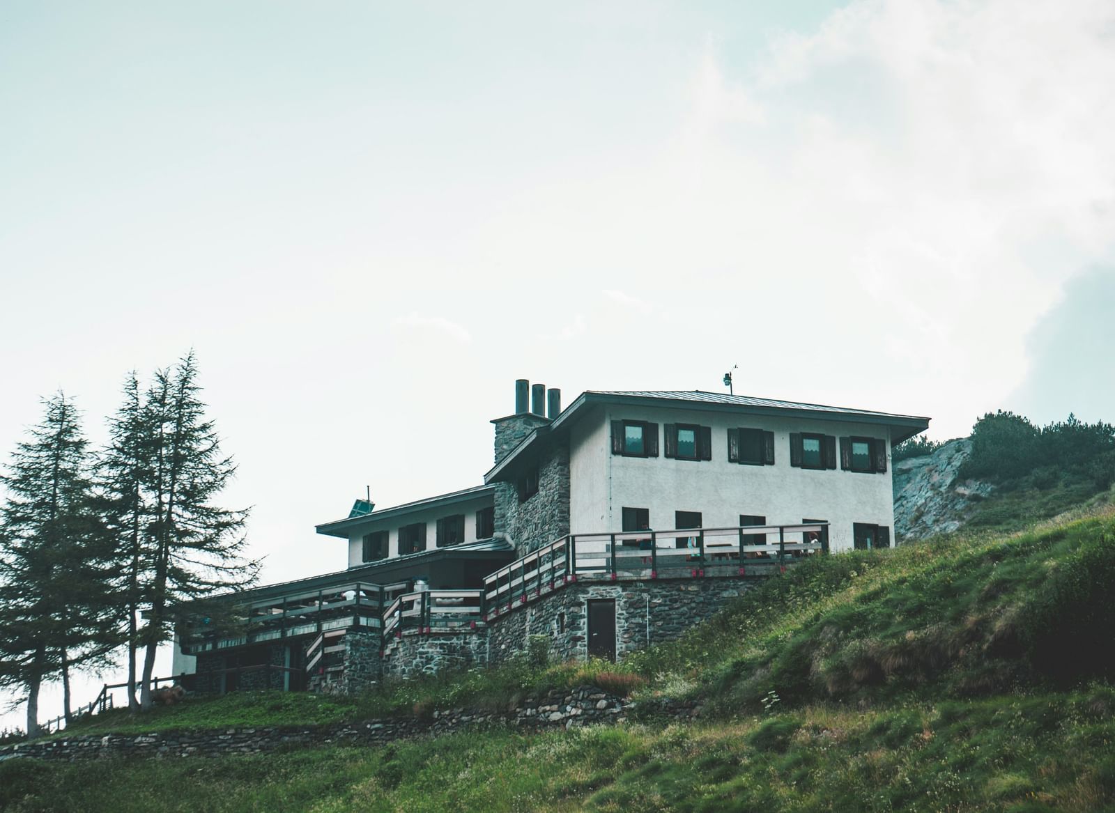A white house sits atop a steep green grassy hill under a bright turquoise sky with soft clouds.