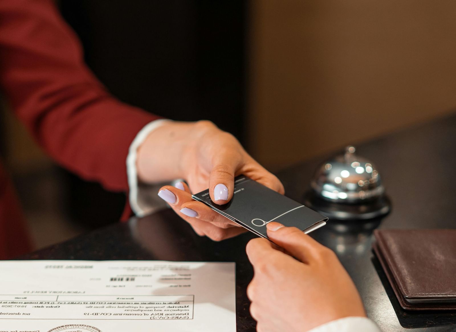 Two hands exchanging an object with a paper, bell, and a table in the background.