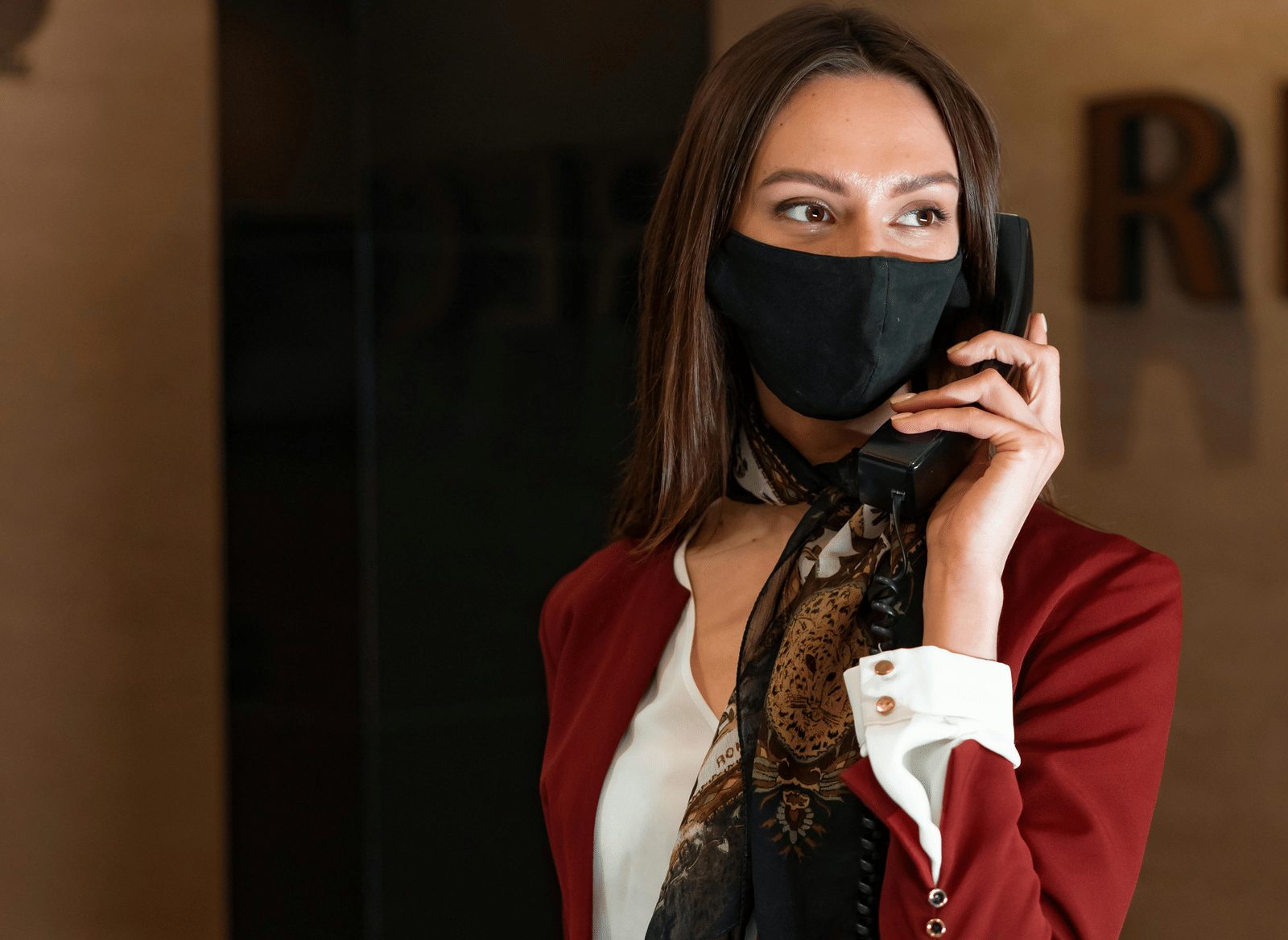 A person wearing a mask holding a telephone to her ear, and a paper in her other hand.