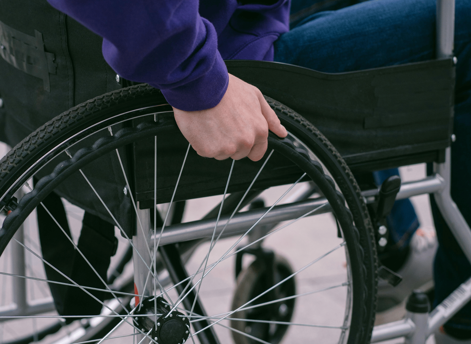 A hand holding the wheel of a wheelchair on grass.