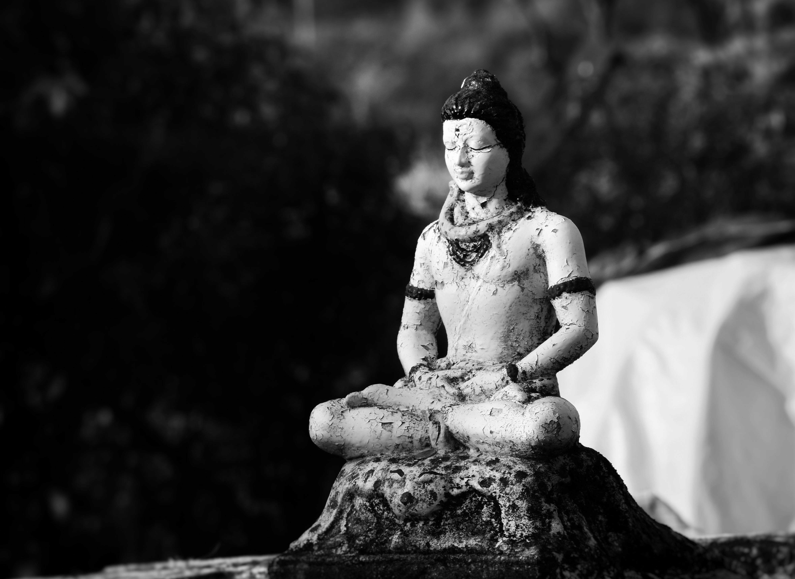 A Black and white image of a Lord Shiva idol kept on a rock.