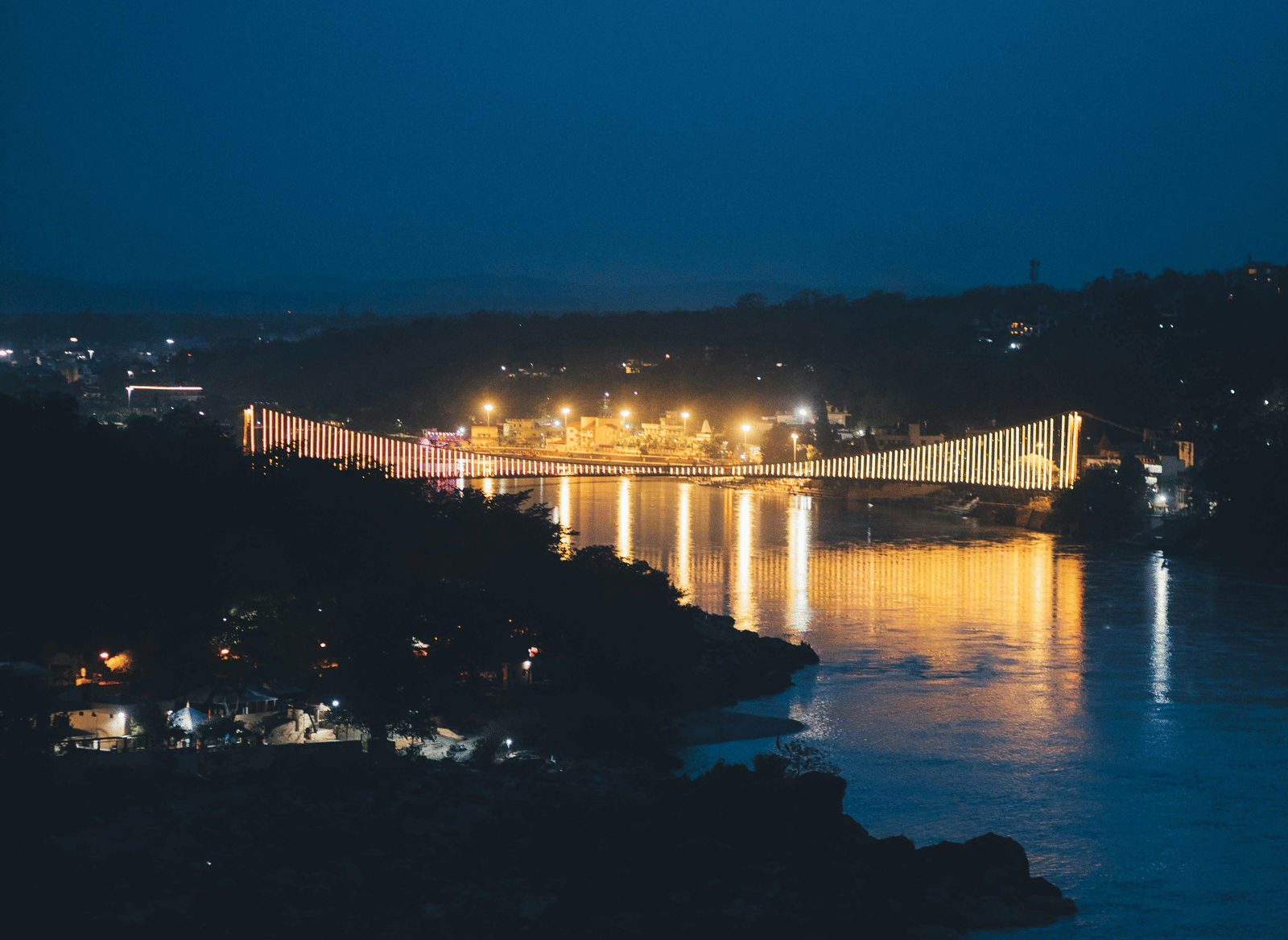A reflection of a bridge is visible in water at night.