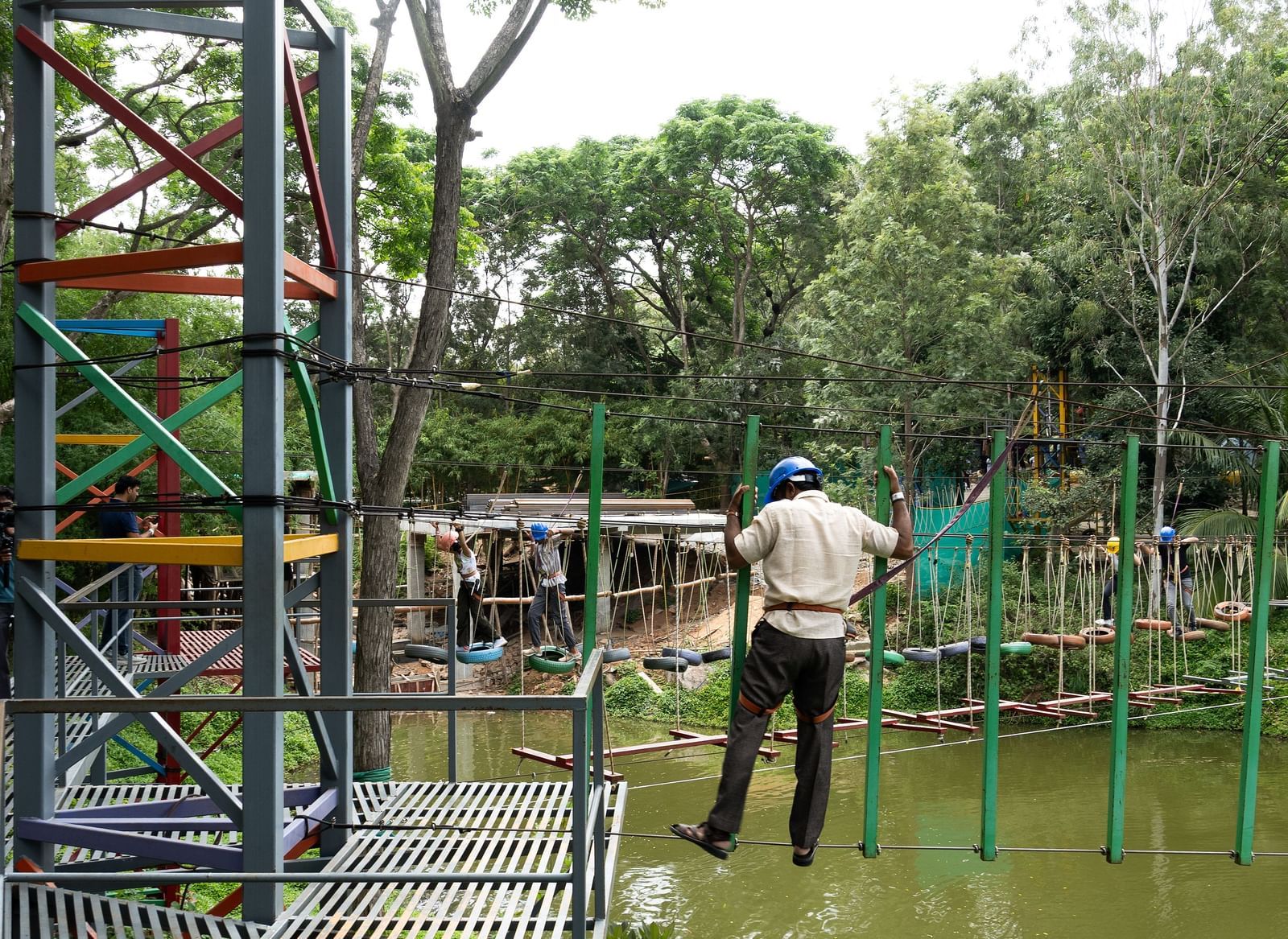 Two people are visible on an outdoor adventure course with ropes and wooden structures in a green environment | RD's Nature Retreat, Bangalore