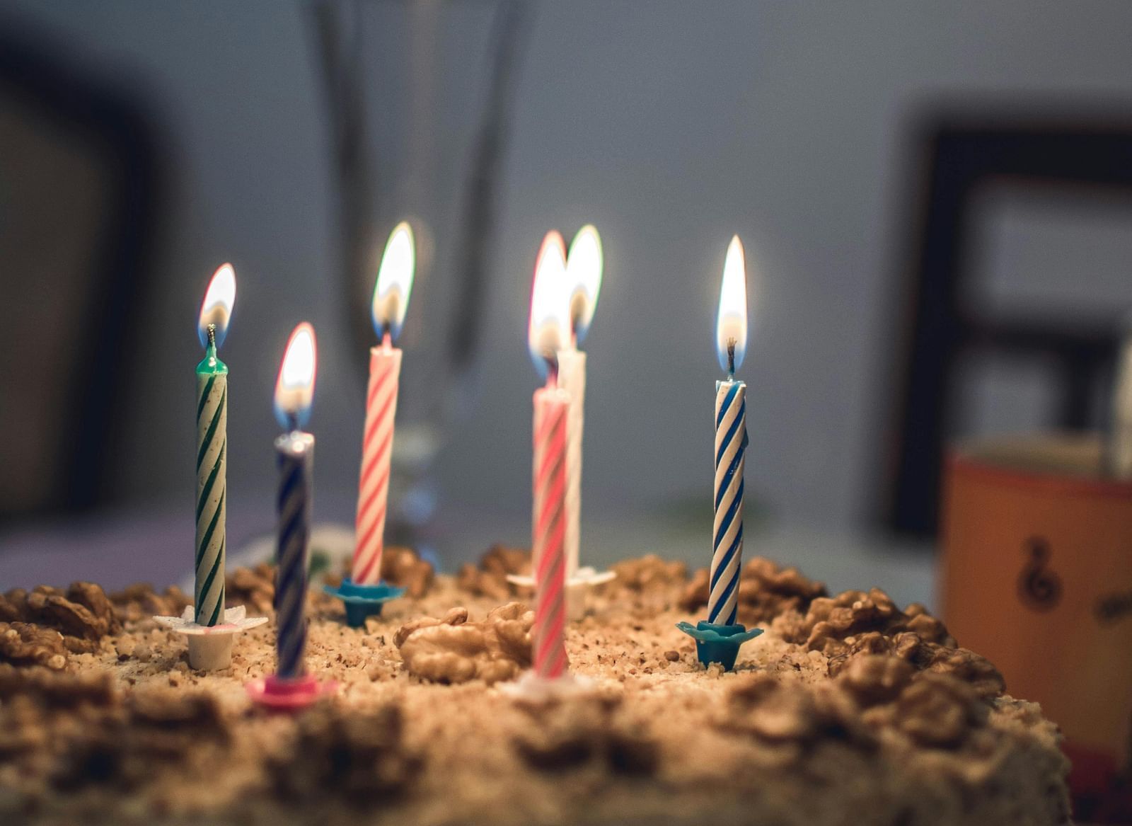 Birthday cake with candles of various colours lit on them with comparatively dark background.