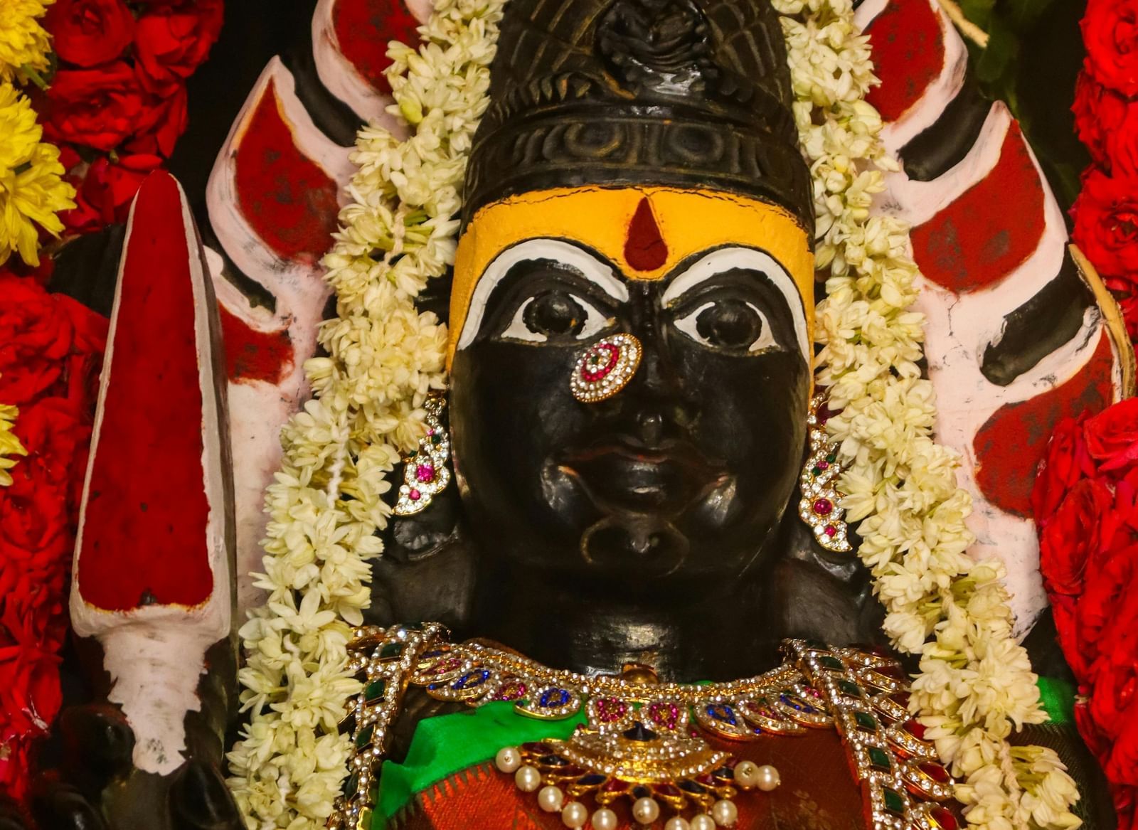 A close-up, vertical shot of a Hindu goddess idol, adorned with colourful garlands and jewellery.