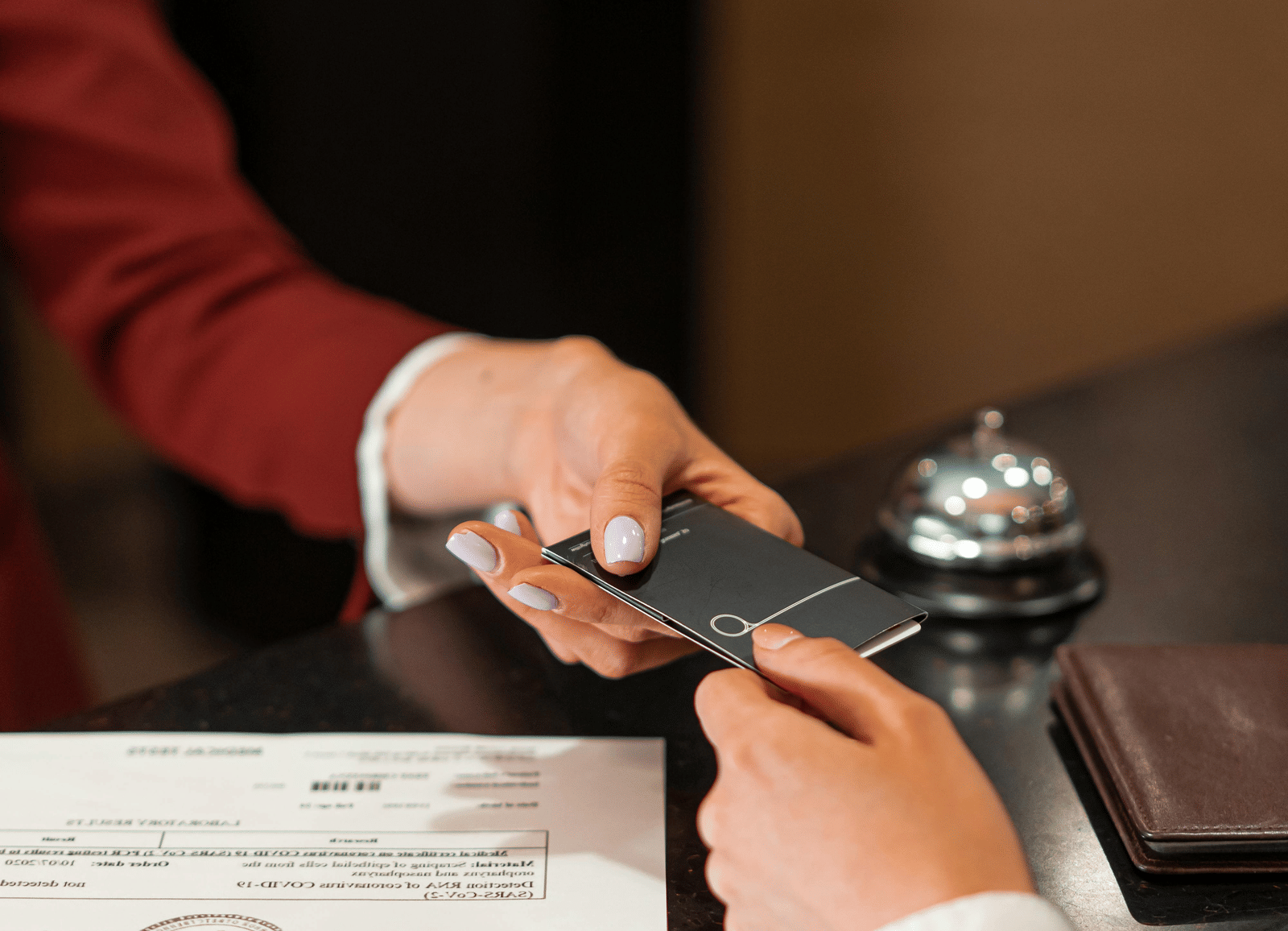 A hotel employee in a red jacket handing a key card to a guest at the reception desk.
