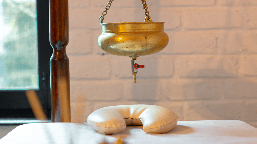 Close-up of a traditional brass Shirodhara pot hanging over a massage table for Ayurvedic treatment - Johnson Lodge & Spa, Manali