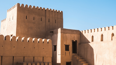 An exterior view of a fort with the sun's rays providing shade near the entrance and blue sky in the background
