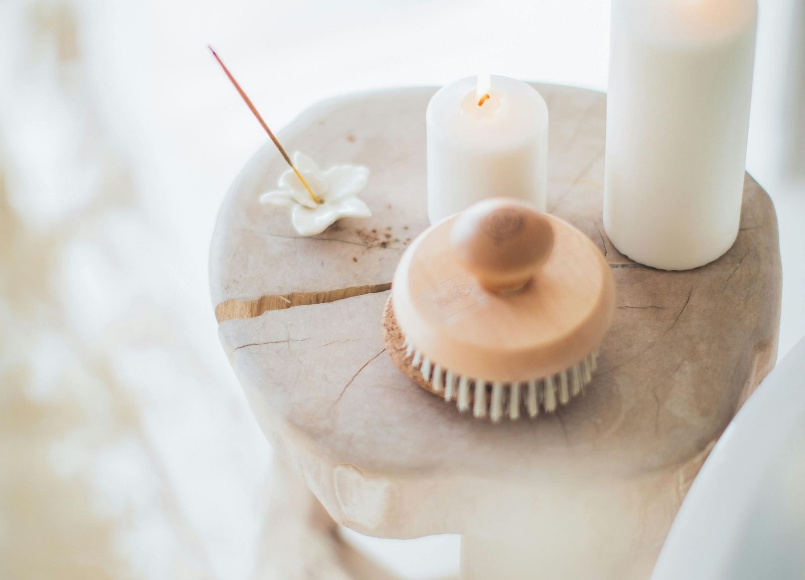 An incense stick, candles and a massaging brush placed on a wooden table in a spa