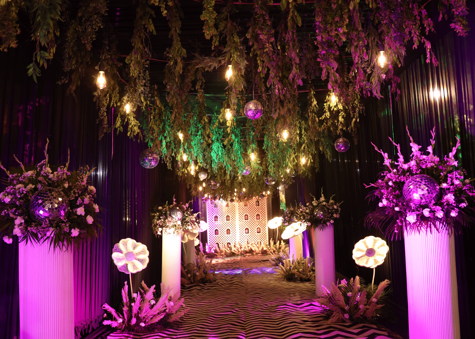 A lavish party entrance archway decorated with purple uplighting and hanging foliage - Megha Resort & Villas, Dehradun