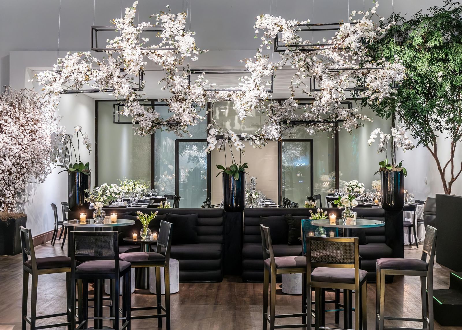 Brightly lit indoor event space with small tables, chairs, and floral decorations.