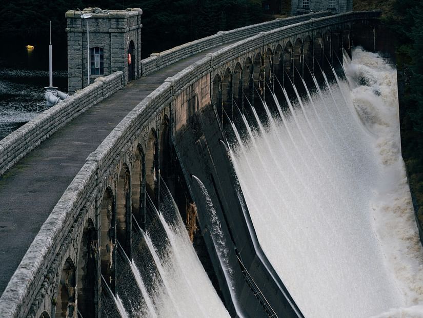 Dam gate with water flowing on one side and still water on the other side with greenery in the distance.