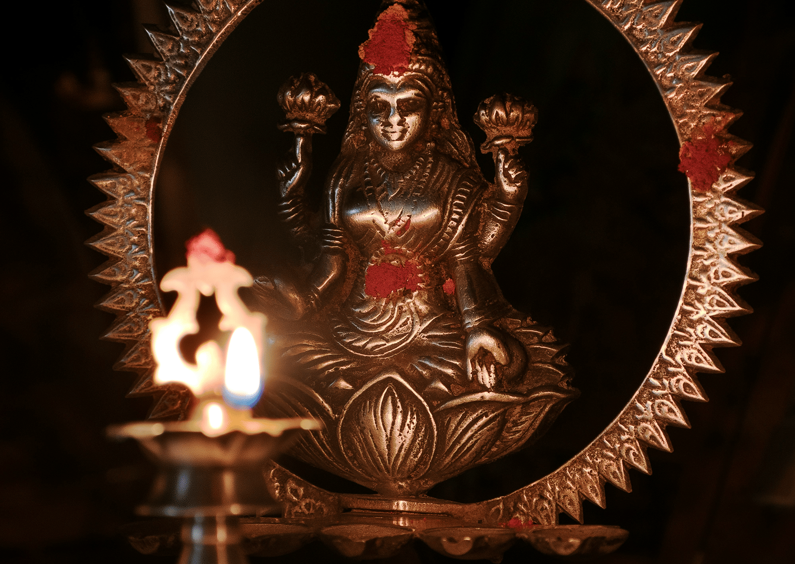 A statue of Goddess Lakshmi placed in front of an illuminated lamp.