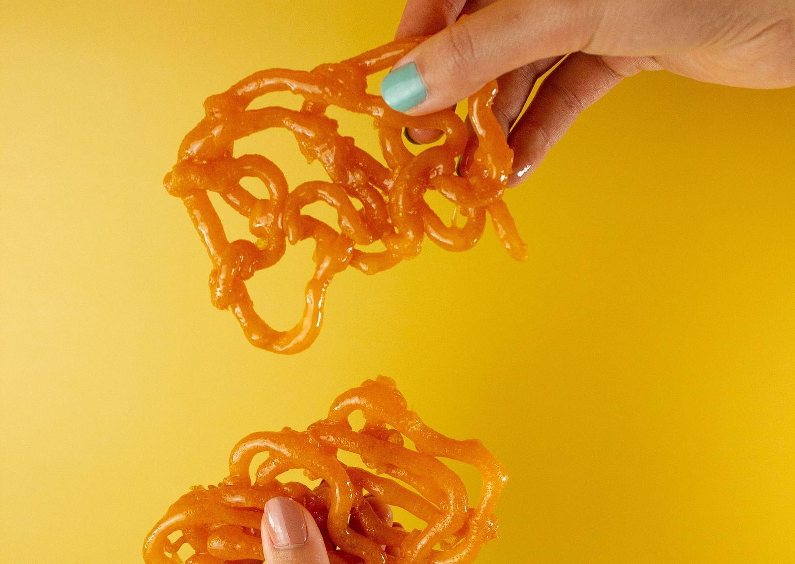 A close up shot of a woman holding jalebi in both her hands and posing for a picture.
