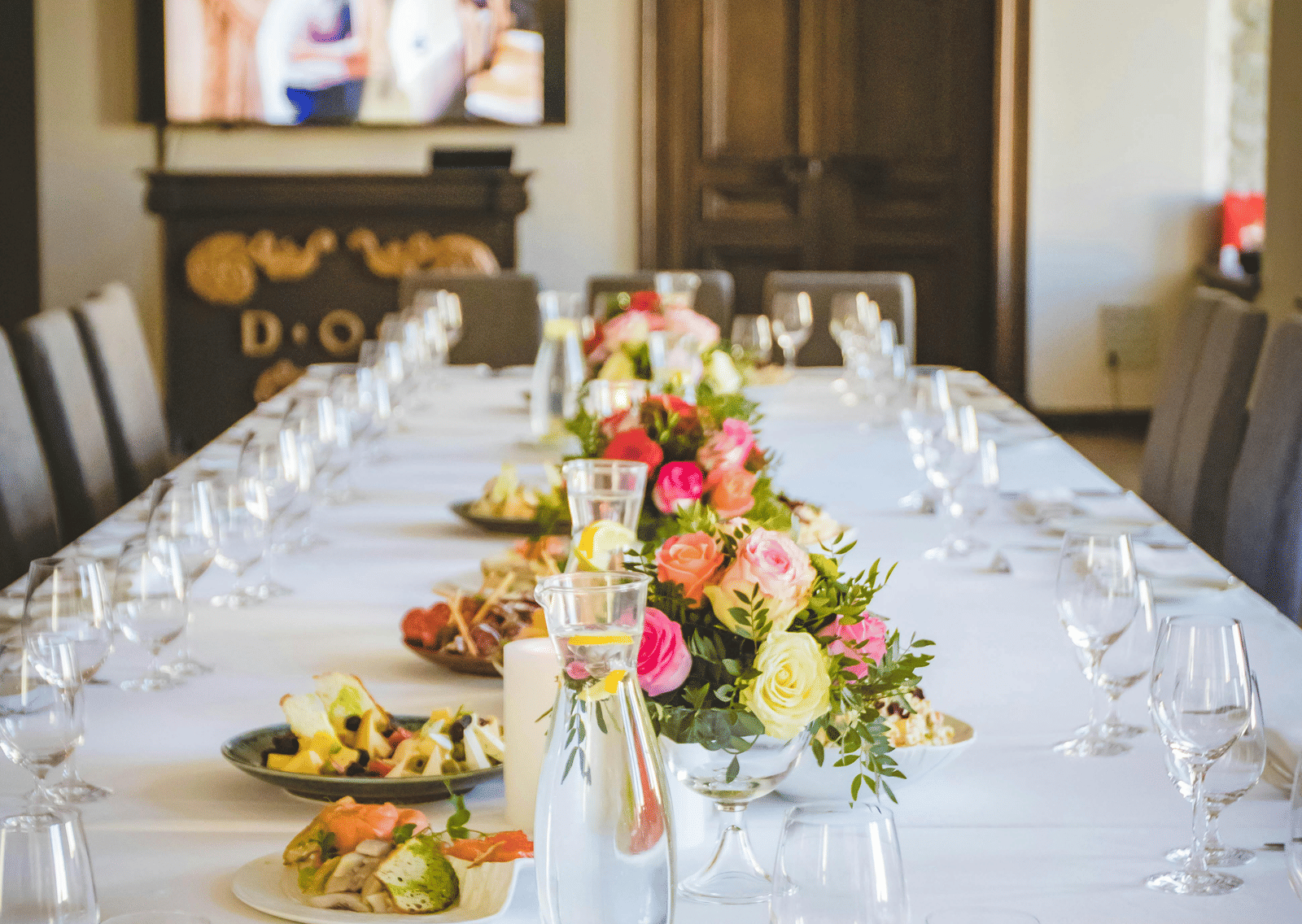 A long dining table decorated with flowers in the middle along with shiny glassware and cutlery set on the table.