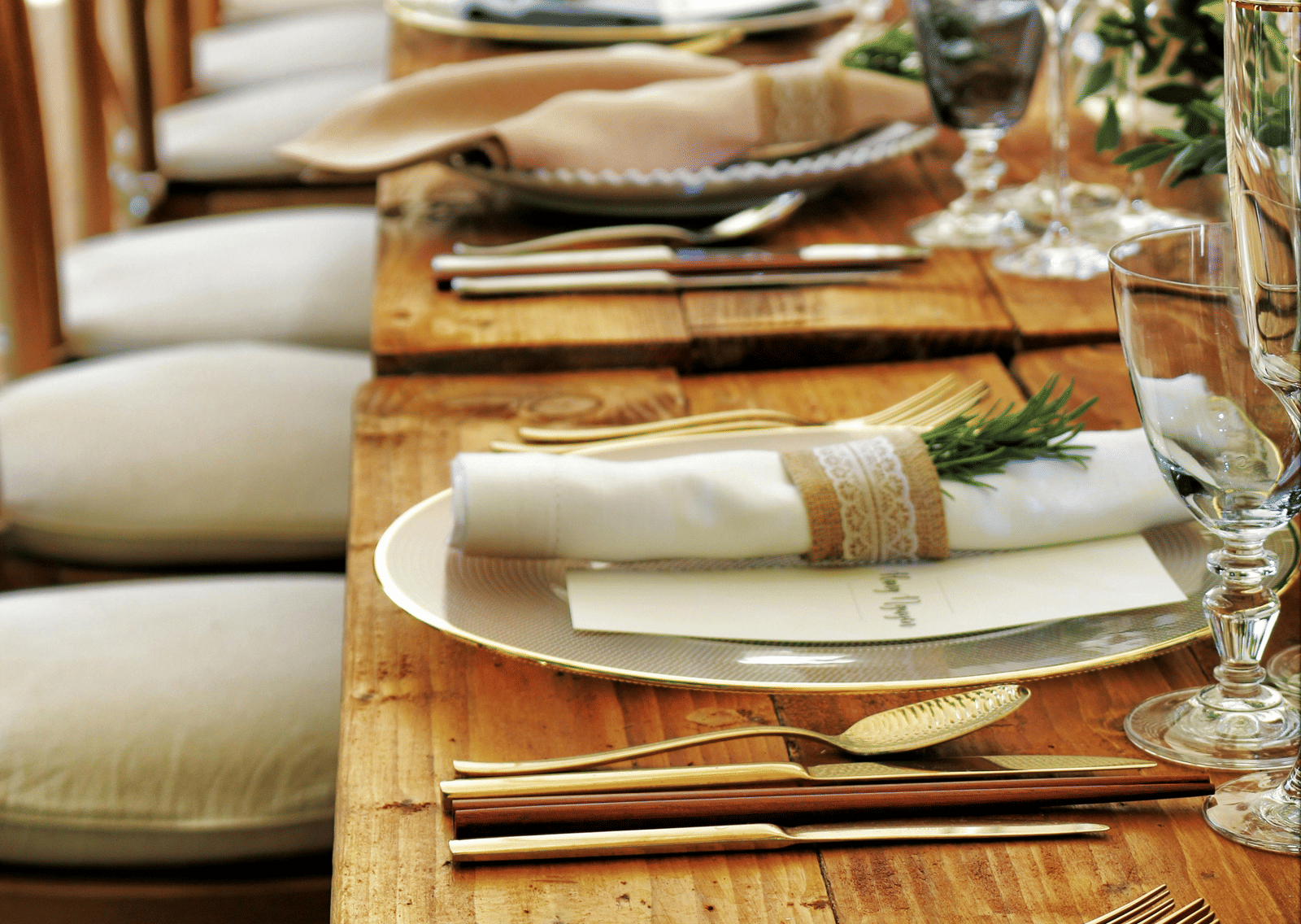 A long wooden table with beautifully set cutlery with small fern leaves in vases.