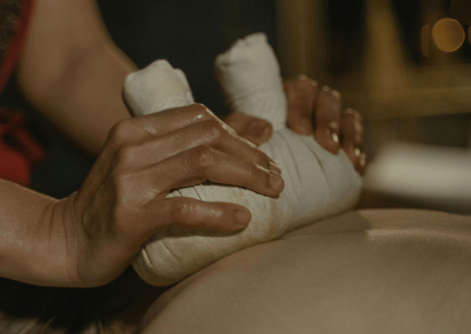A masseuse using cloth bundles to press the back of a person.