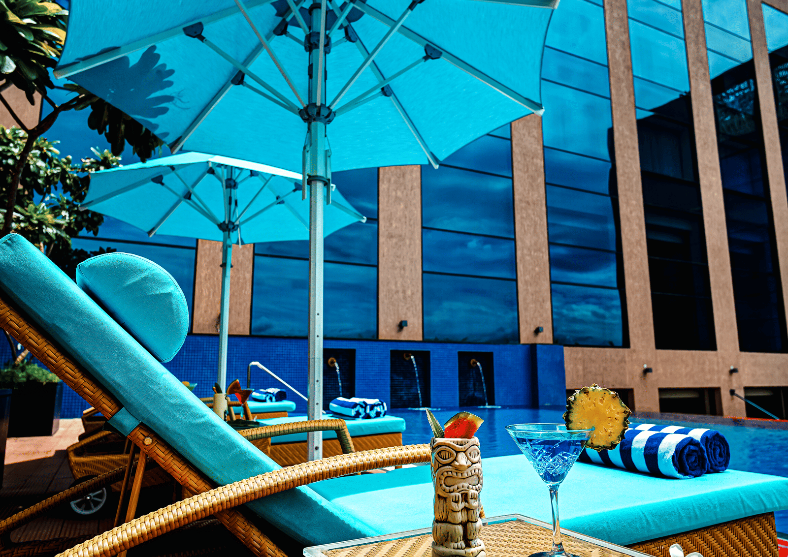 Brightly lit poolside with comfortable sun loungers and a refreshing drink, offering an ideal spot for relaxation - Grand Madurai by GRT Hotels
