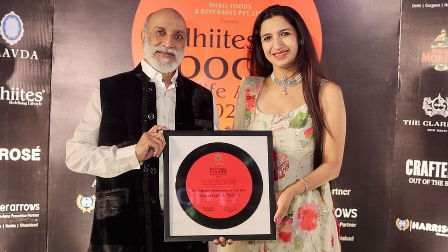 Two people posing with a framed award for 'Pet-Friendly Destination of the Year 2025' awarded to Tijara Fort & Palace at the Delhiites Food & Nightlife Awards.