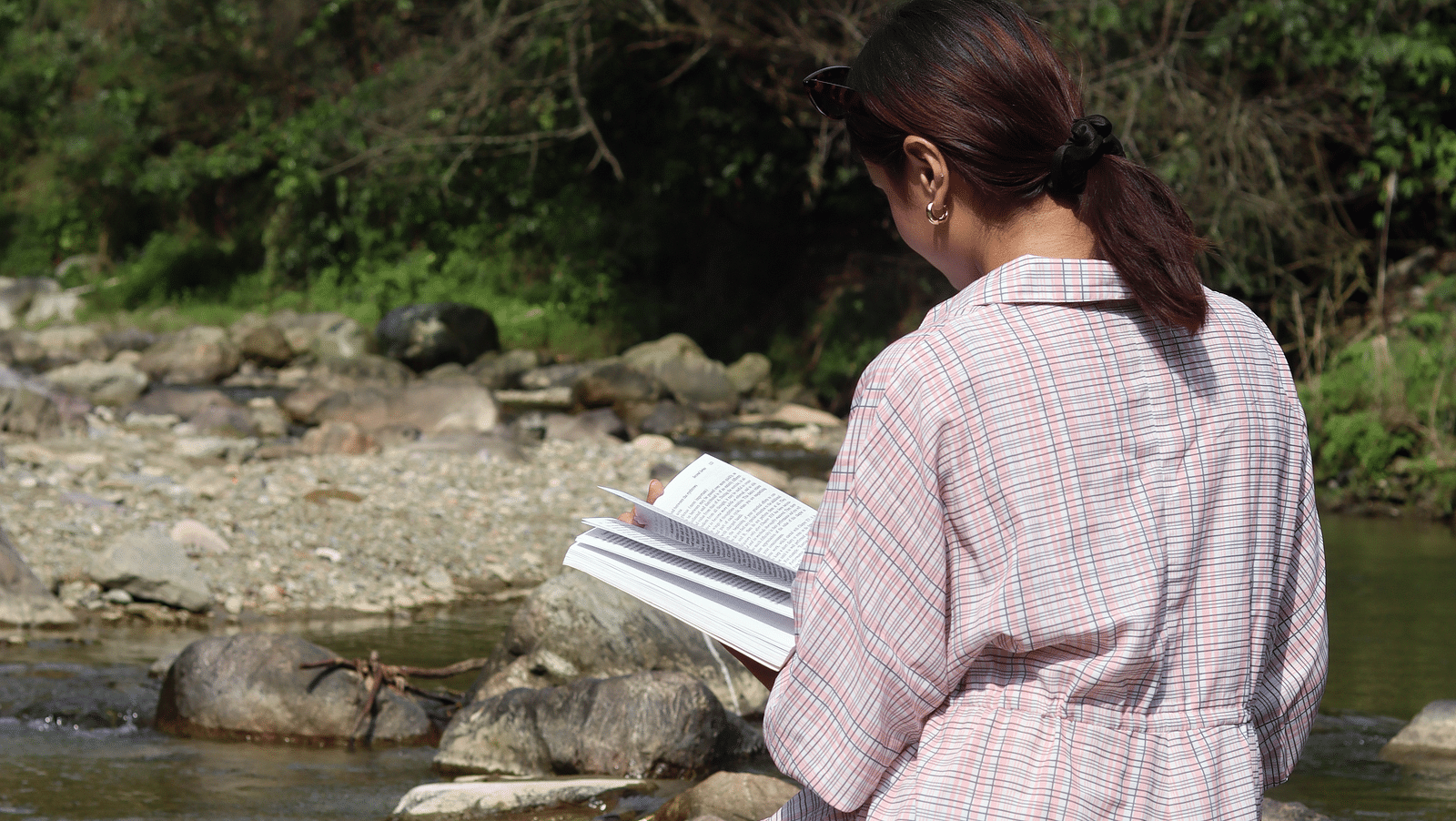 A woman reading a book sitting by the stream at A man flying a kite at The Sylvan Retreat, Dehradun.