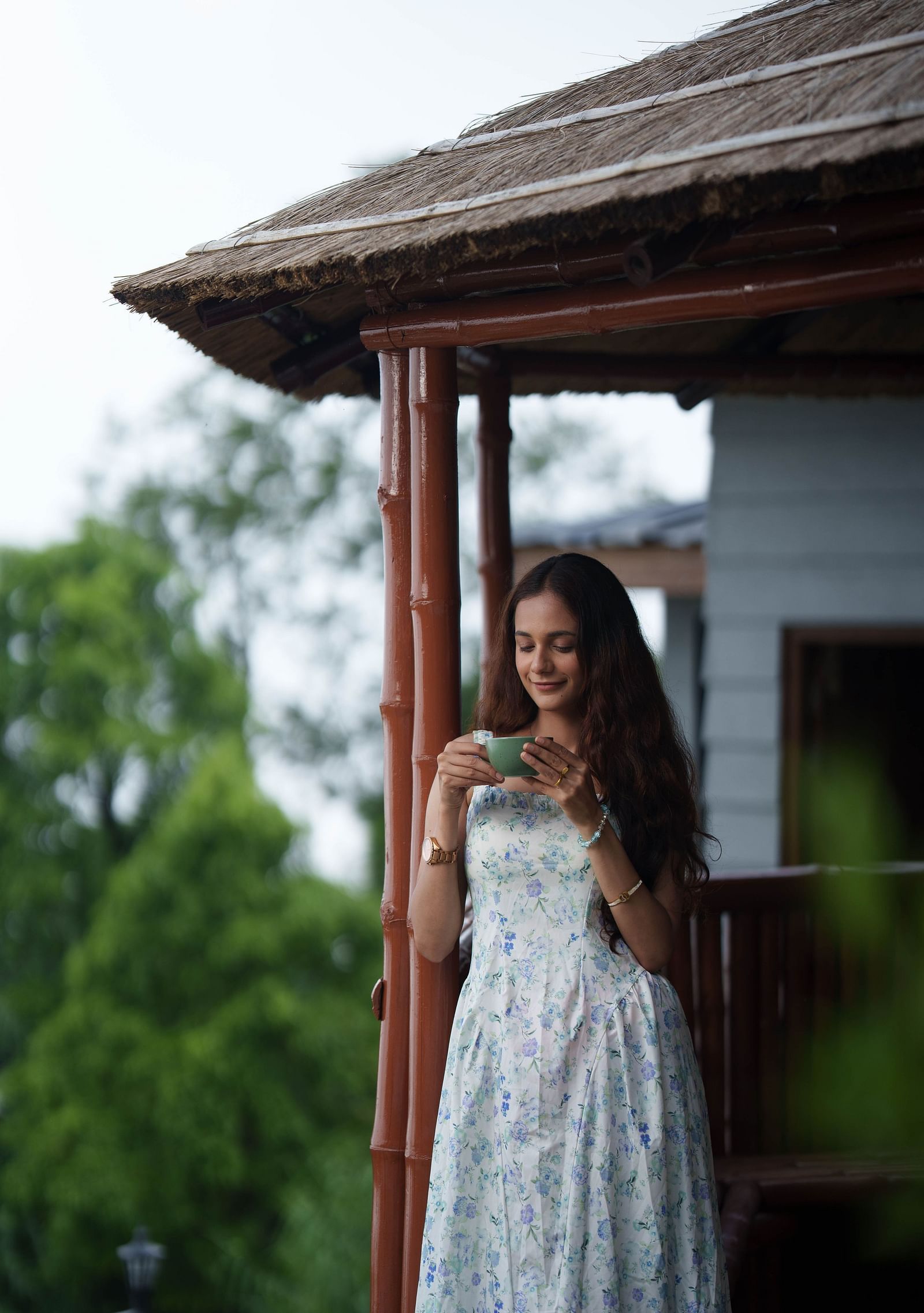 A woman in a white dress stands outside a small wooden gazebo or structure, looking out, at Summit Enigma Resort and Spa.