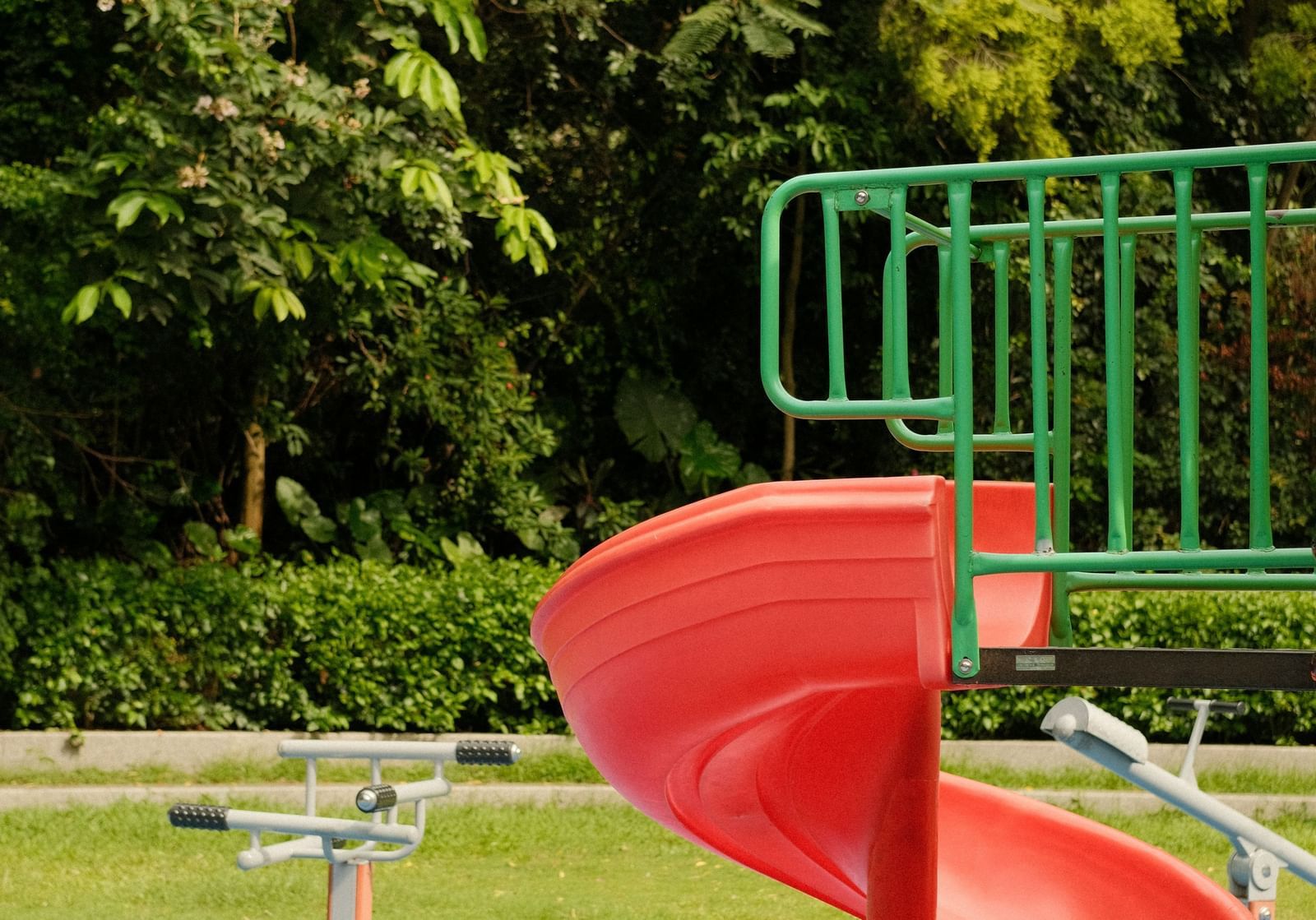Red spiral slide in an outdoor playground surrounded by greenery.