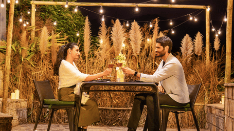 Candlelight dinner setup at Polo Resort Cherrapunji with couple toasting wine under string lights, pampas grass and stone patio.