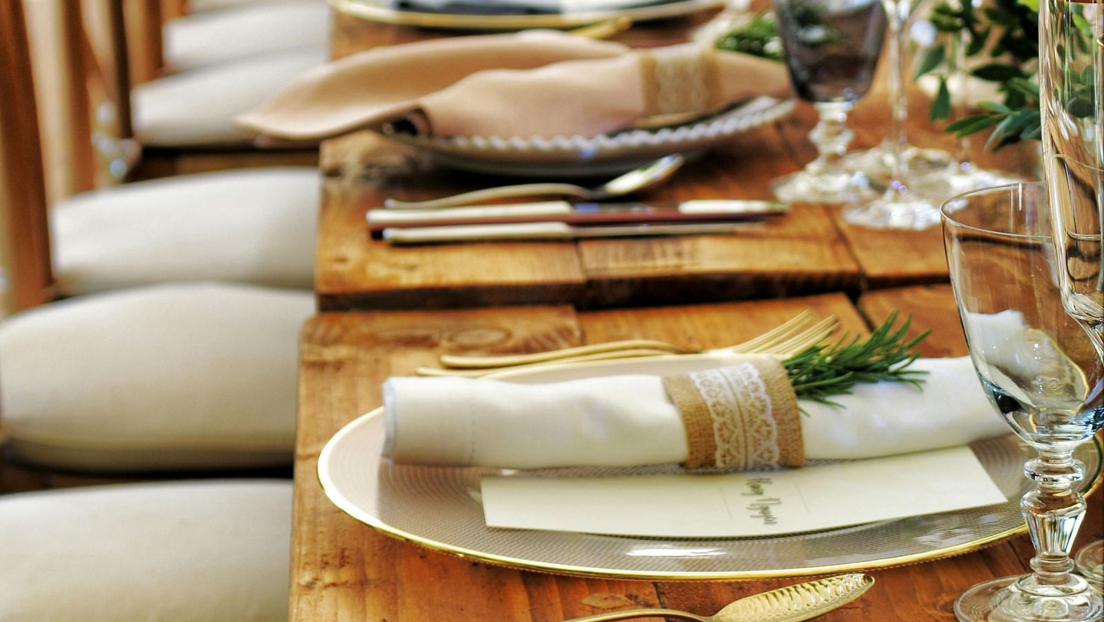 a long wooden table with beautifully set cutlery with small fern leaves in vases
