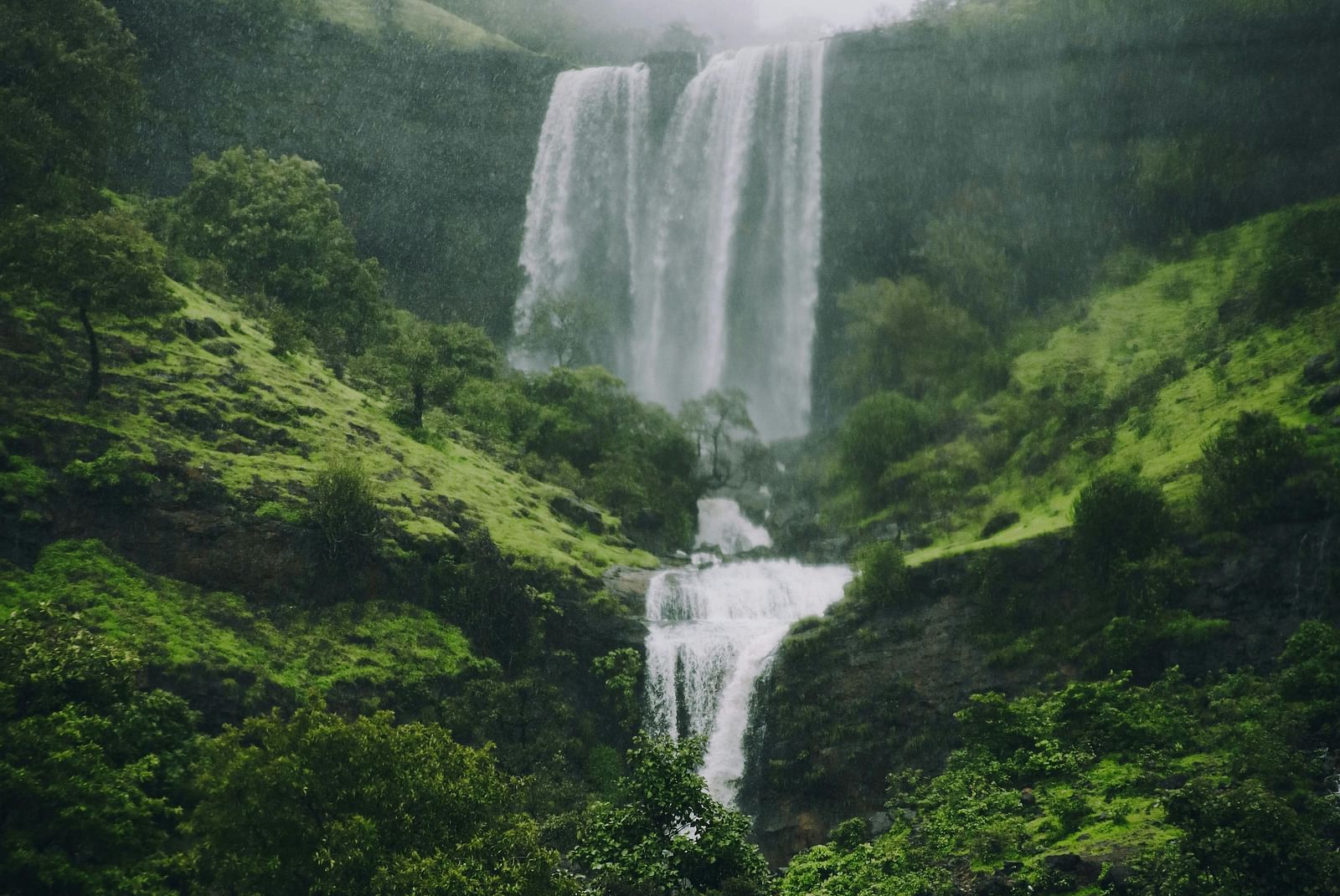 A misty waterfall cascading down a lush green hillside, located in Igatpuri.