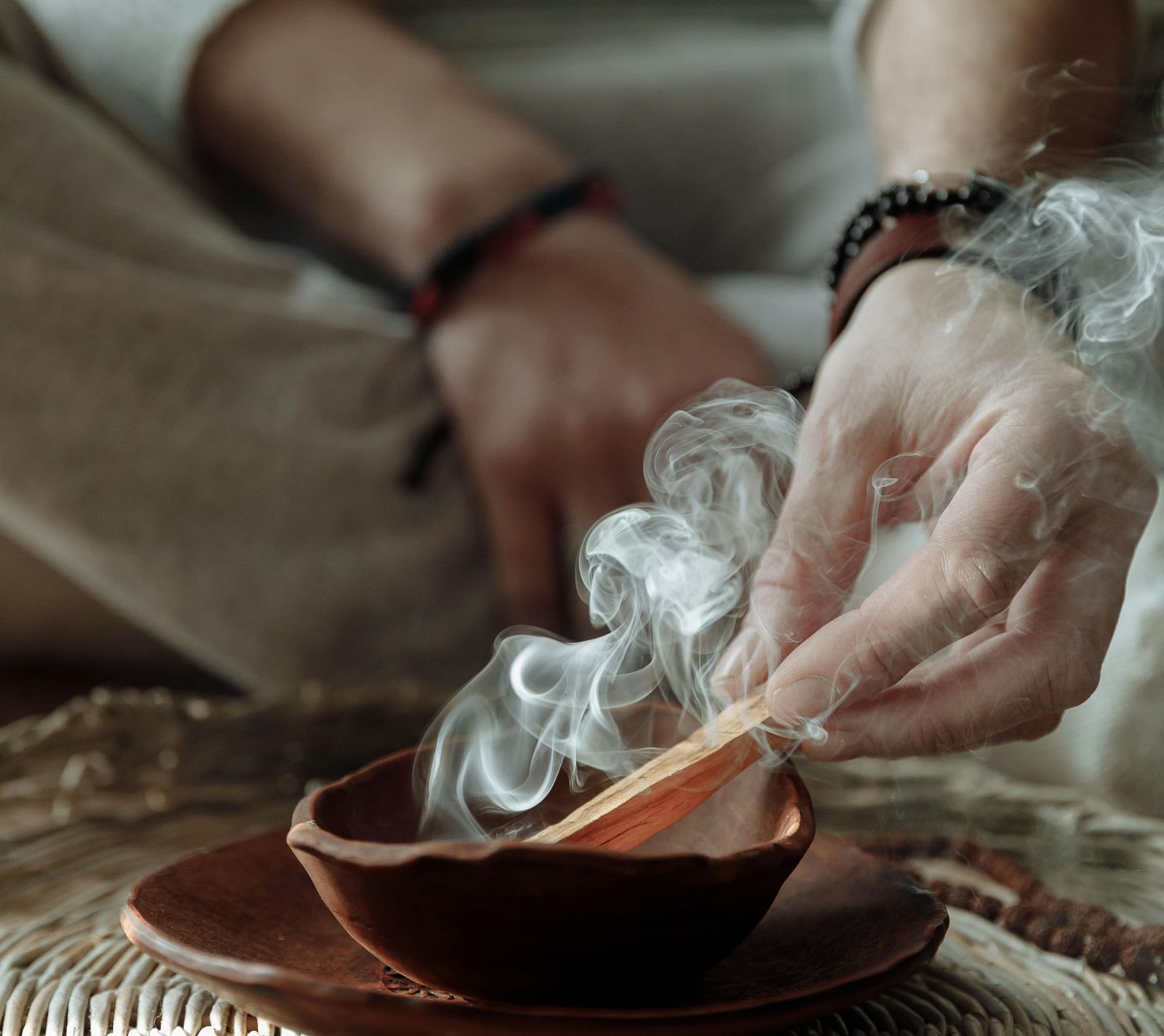 A person sitting on a huge mat burning incense sticks into a bowl.