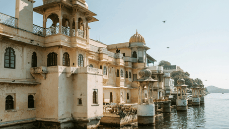 Historic waterfront houses in Udaipur reflected in the calm lake water.