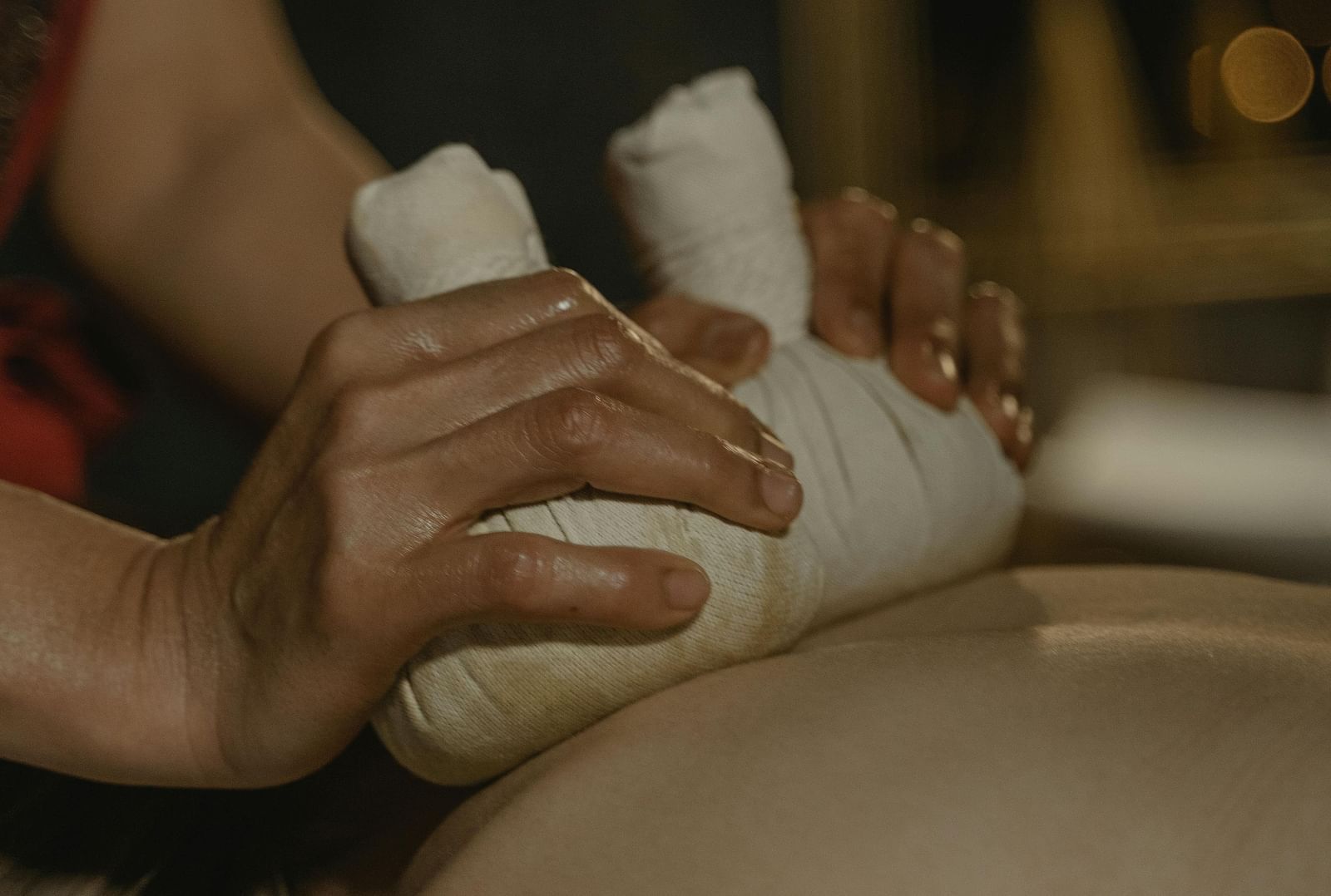 A masseuse using cloth bundles to press the back of a person.