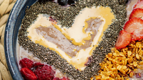 A breakfast bowl topped with raspberries, blueberries, and seeds on a woven mat.