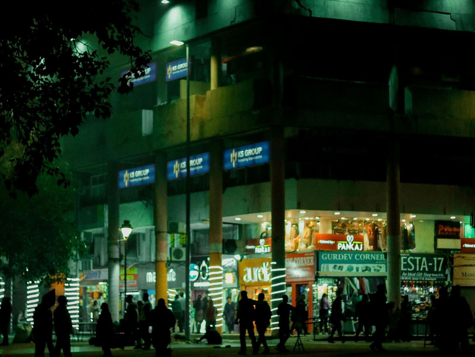 Facade of a shopping mall at night with people walking around in front of it.
