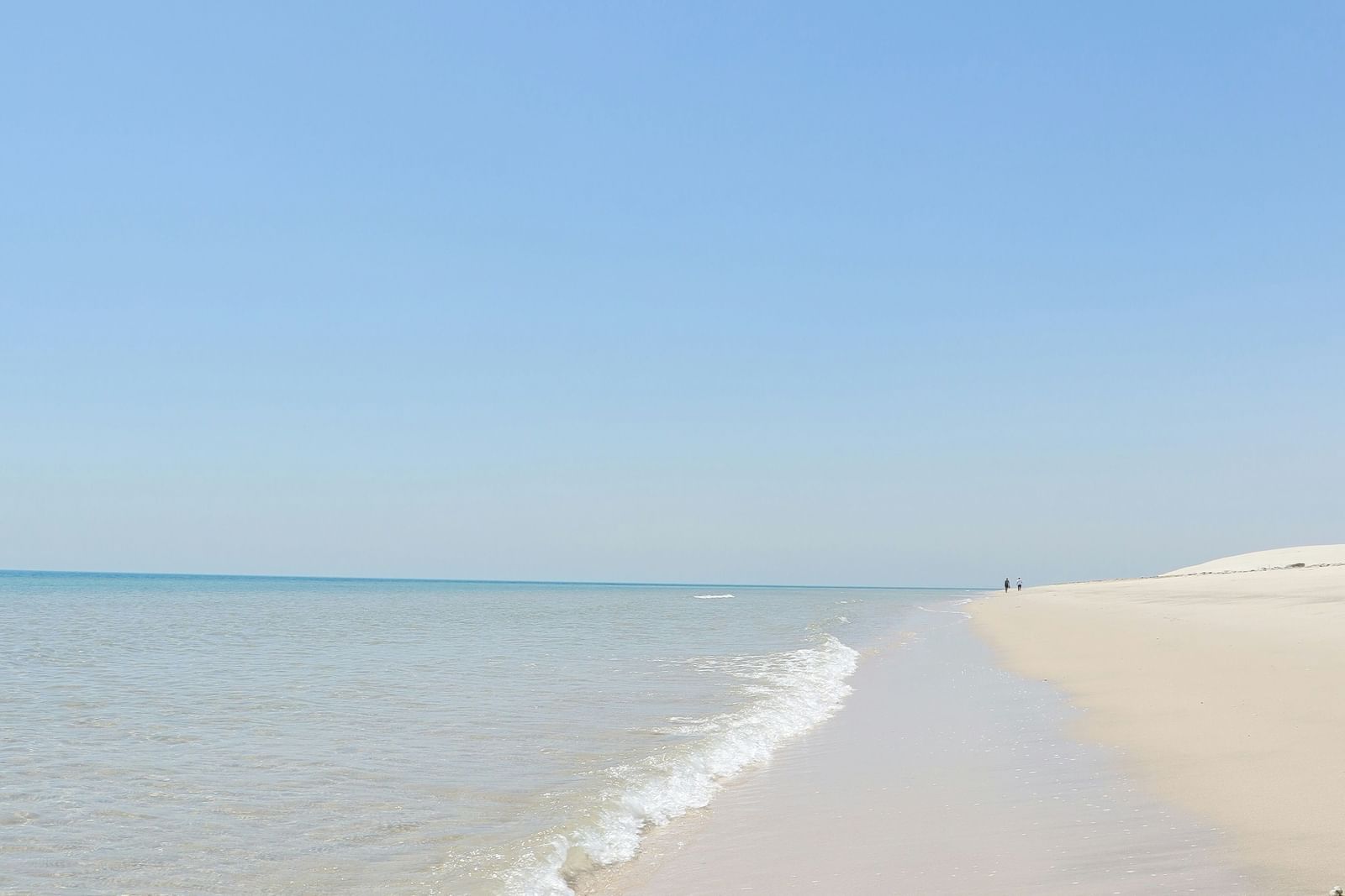  A calm, clear blue sky over a tranquil sandy beach with gentle waves lapping the shore.