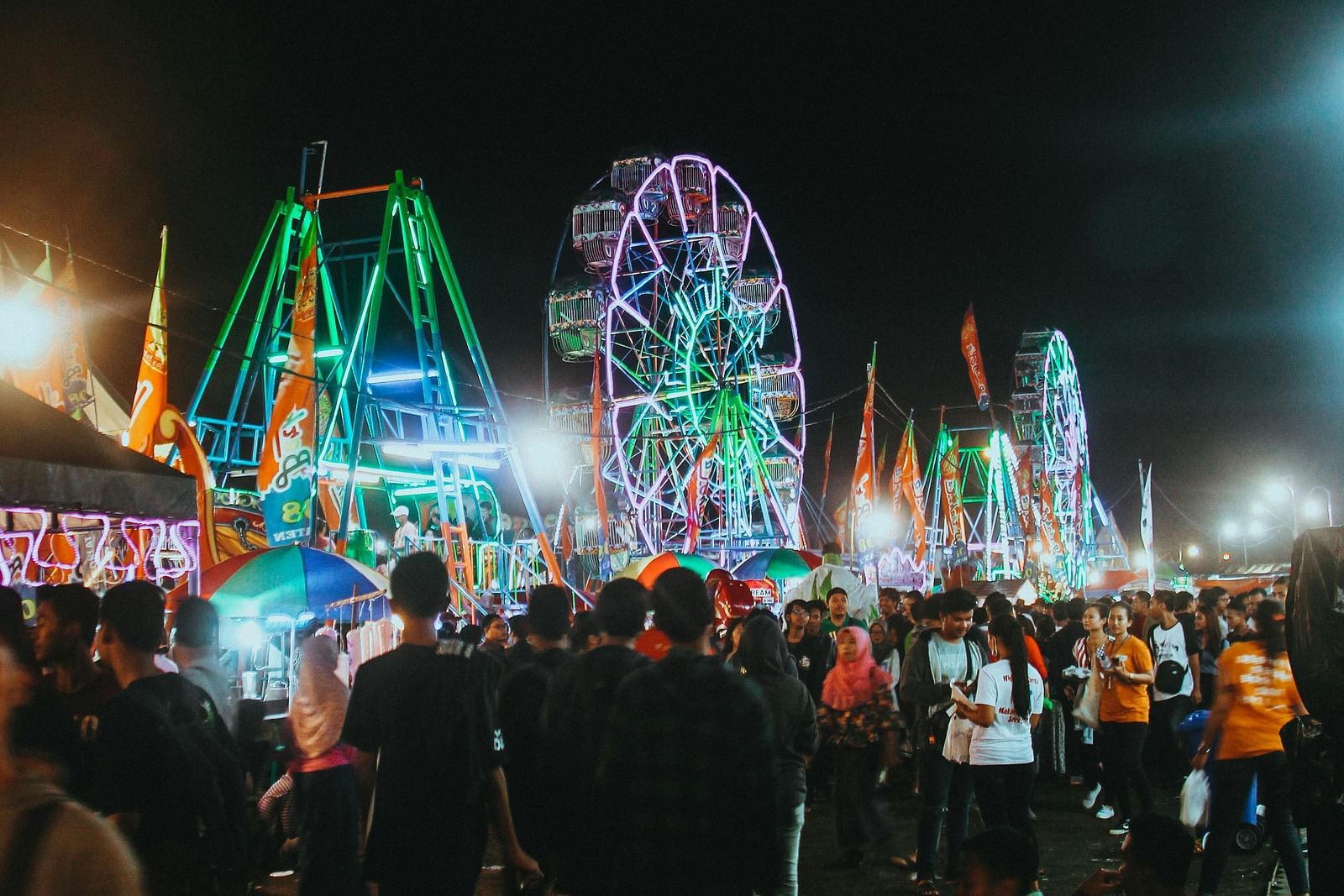 image of a fair in a night time featuring various rides and a huge crowd that has come to enjoy it
