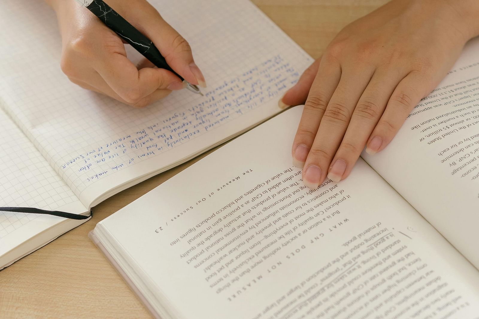 image of a person referring a book and writing something in a notebook with pen