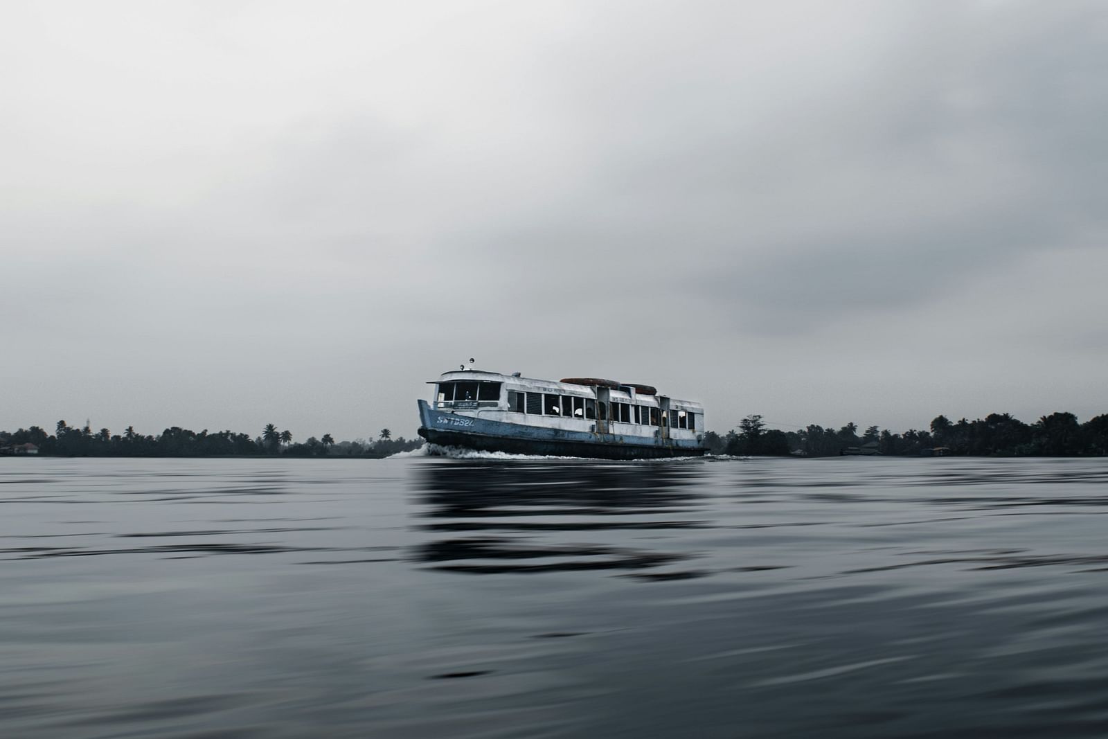 A solitary boat travelling on Vembanad lake in Kumarakom with white clouds in the sky.