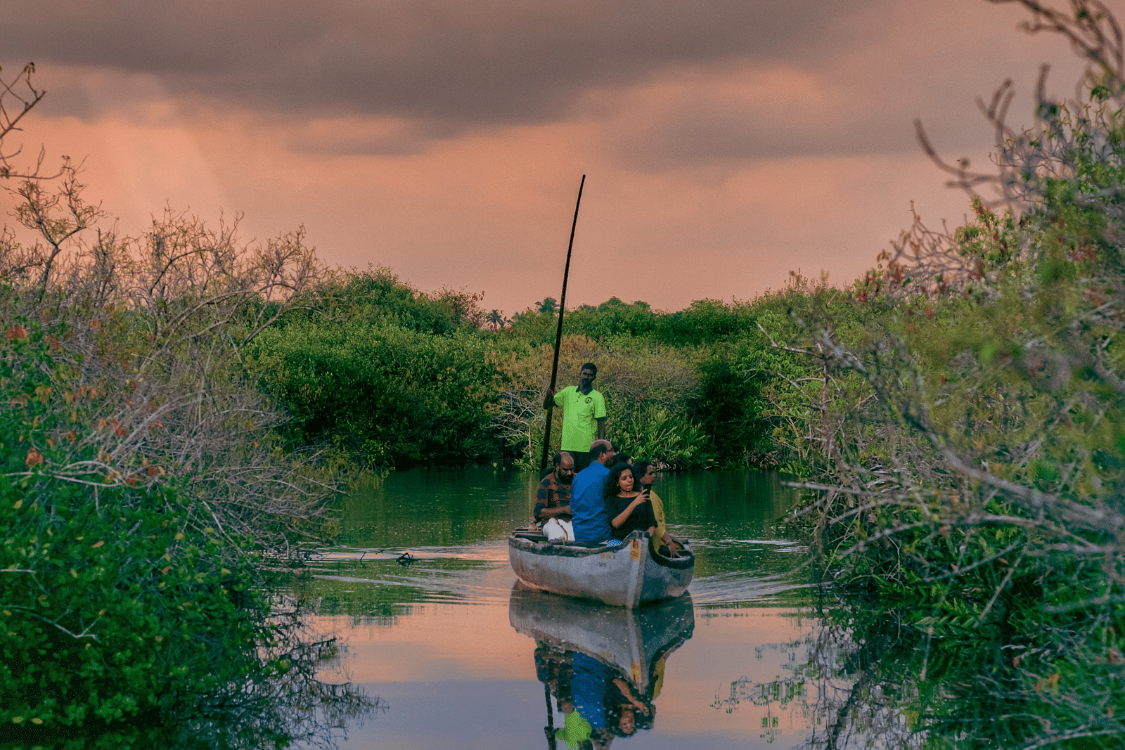 A lone canoeist navigating through a calm water channel reflecting the colours of the sunset - Kumarakom